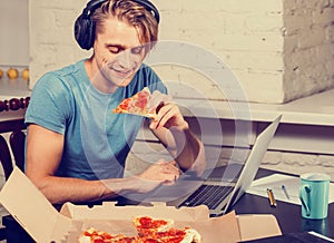 Young man eats pizza using laptop surfing internet