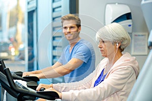 Young man and elderly lady using exercise machines