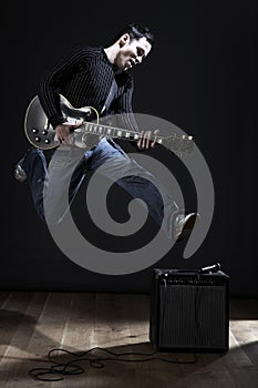 Young man with electric guitar jumping on stage