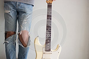 A young man with an electric guitar Leaning against a cement wa