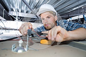 young man electrician wiring inside ceiling