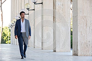 Young man in elegant suit walking outdoors with a building as a background. Columns of white marble. White shirt and jacket photo