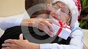 Young man embracing his senior mother and giving Christmas present. Mother hugging son Christmas eve. Elderly woman