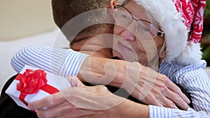 Young man embracing his senior mother and giving Christmas present. Mother hugging son Christmas eve. Elderly woman