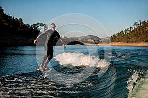 young man energetically balancing on river water on a foil wakeboard on beautiful landscape background.