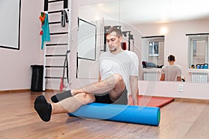 Young man is engaged in kinesiotherapy with the help of a roller