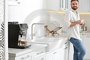 Young man enjoying fresh aromatic coffee in kitchen, focus on modern machine