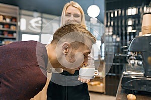 Young man enjoying fresh fragrant coffee, drinking coffee from a cup in the hands of girl barista