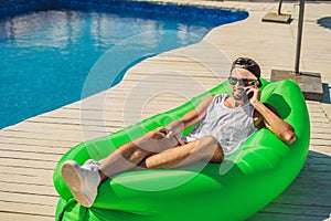 Young man enjoying leisure, lying on the air sofa Lamzac, near the pool