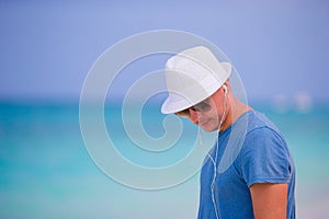 Young man enjoying the music on white sandy beach. Happy tourist relaxing on summer tropical vacation.