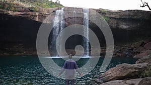 Young man enjoying the natural waterfall falling from mountain top at morning