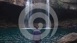 Young man enjoying the natural waterfall falling from mountain top at morning
