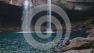 Young man enjoying the natural waterfall falling from mountain top at morning