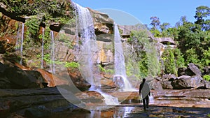 Young man enjoying the pristine natural waterfall falling from mountain top at day from low angle