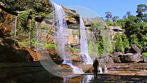 Young man enjoying the pristine natural waterfall falling from mountain top at day from low angle