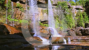 Young man enjoying the pristine natural waterfall falling from mountain top at day from low angle