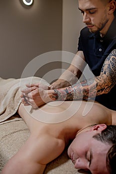 Young man enjoying relaxing body massage in spa salon or massage room. Qualified specialist massaging male patient