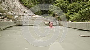Young man enjoying thermal bath in outdoor spa resort. Handsome man bathing in mineral water pool. Natural spa complex