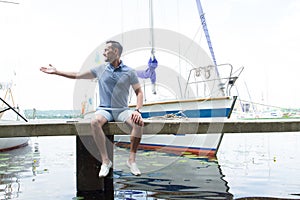 Young Man enjoying time at riverside marina, sitting on pier. young man relax docks at the pier by the harbor