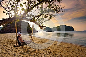 Young man enjoys sunset on a swing at a beach in Thailand