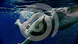 Young man enjoys swimming underwater in the clear lake