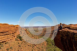 Young man enyoing view of a Canyon and sitting on the edge of a cliff, Watarrka National Park, Northern Territory, Australia