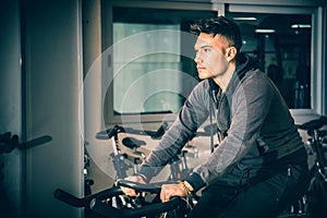 Young man exercising in gym: spinning on stationary bike