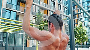 Young man exercising outside. Muscled powerful guy doing pull ups on street. Camera moves after him up and down. Sports
