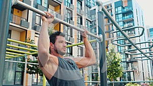Young man exercising outside. Static camera. Guy doing pull up exercises with his strong arms. Doing sports activity on
