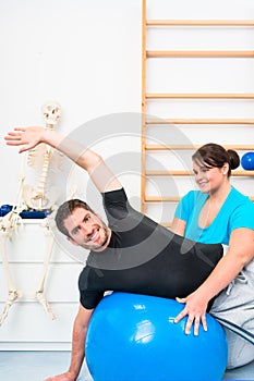 Young man exercising on swiss ball in physiotherapy