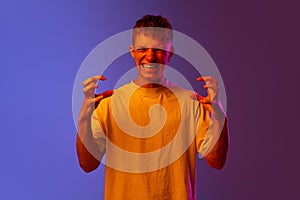 Young man expressing anger, irritation and annoyance against gradient purple background in neon light