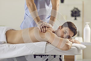 Young man with eyes closed enjoying procedure of medical massage from professional masseur