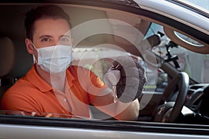 Young man with face mask holding a key in the car, auto mechanic driving customer car to automobile service center
