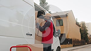 Young man with face mask loading van with cardboard boxes