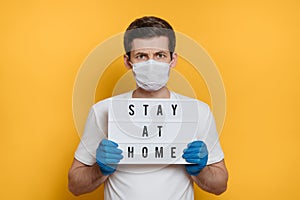 Young man in face mask with Stay home text on yellow background
