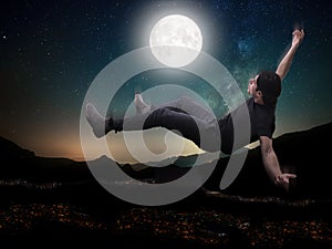 Young man falling in the sky above city in moonlight