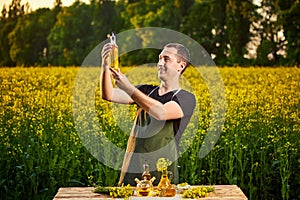 A young man farmer or agronomist examines the quality of rapeseed oil on a rape field. Agribusiness concept