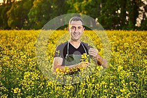 A young man farmer or agronomist examines the quality of rapeseed oil on a rape field. Agribusiness concept
