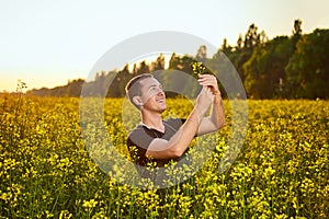 A young man farmer or agronomist examines the quality of rapeseed oil on a rape field. Agribusiness concept