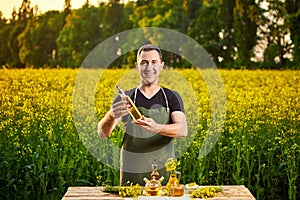 A young man farmer or agronomist examines the quality of rapeseed oil on a rape field. Agribusiness concept