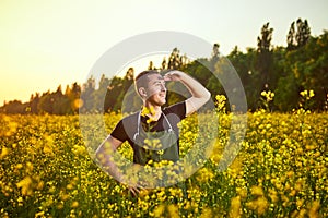 A young man farmer or agronomist examines the quality of rapeseed oil on a rape field. Agribusiness concept