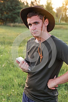 Young man farmer in cowboy hat at agricultural field on sunset holding tablet. Portrait of happy man standing on nature