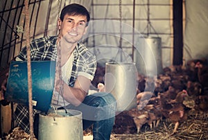 Young man farmer holding bucket in henhouse