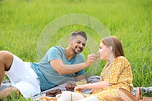 Young man feeding his girlfriend with grape on blanket outdoors