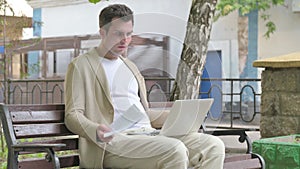 Young Man Feeling Upset while Reading Contract and Using Laptop Outdoor