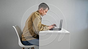 Young man fidgets on chair working via laptop at table