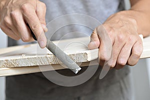 Young man filing a wooden board with a rasp photo