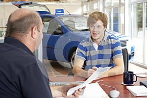 Young man filling in paperwork in car showroom