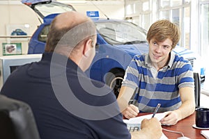 Young man filling in paperwork in car showroom