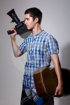 Young man filmmaker with old movie camera and a suitcase in his photo